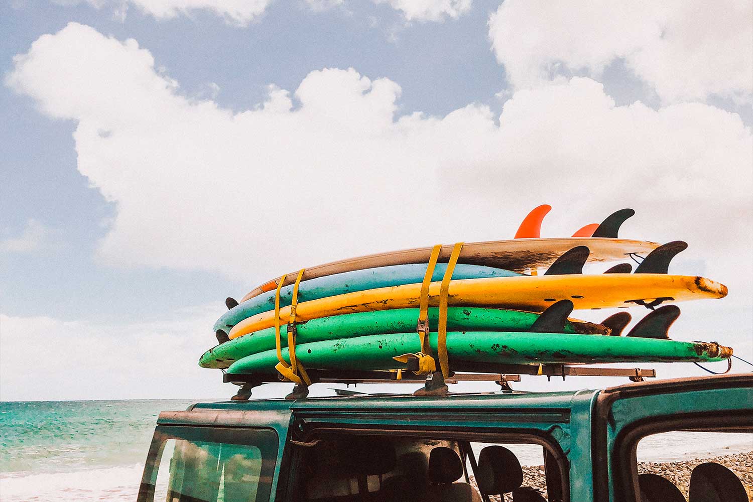 Moodbild eines Kleinbusses mit mehreren Surfbrettern auf dem Dach angebracht im Sommer